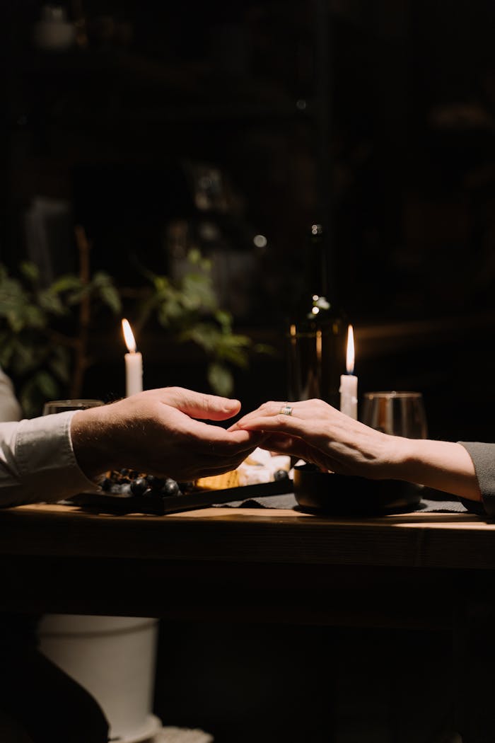 Couple holding hands at a romantic candlelit dinner, creating an intimate atmosphere.